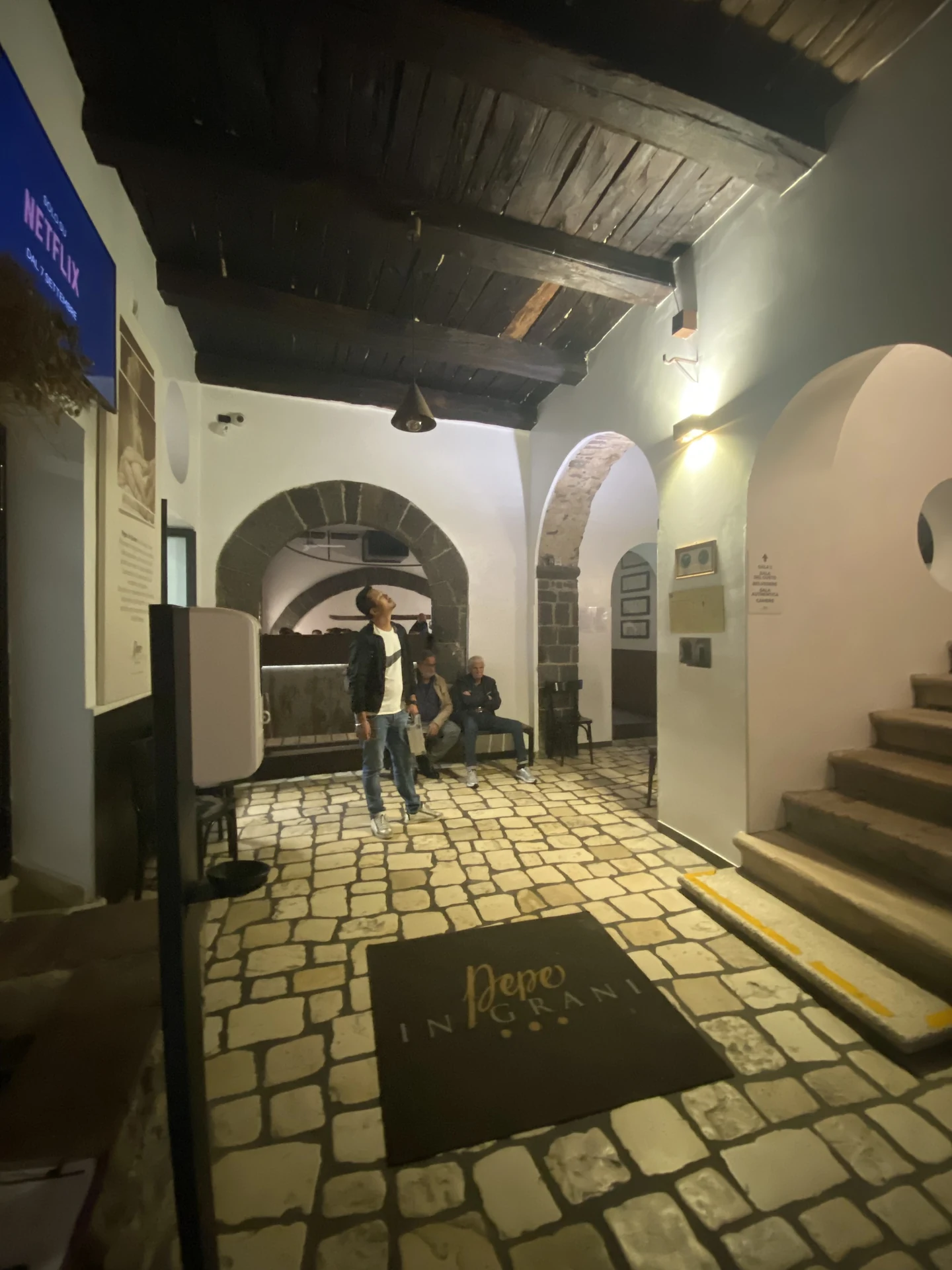 Atrio storico interno di Pepe in Grani con pavimentazione in pietra, archi e travi in legno illuminate da applique calde