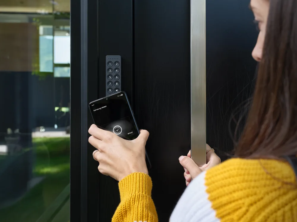 Persona che avvicina lo smartphone al tastierino Nuki Keypad 2 NFC per aprire la porta
