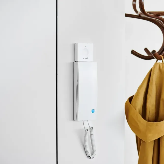 Nuki Opener bianco montato sul citofono a parete in un ingresso, per aprire il portone dallo smartphone