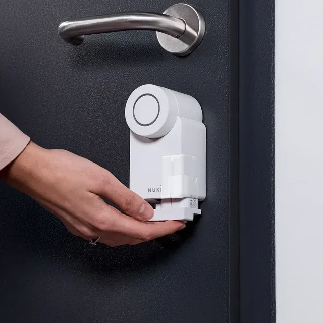 Mano che inserisce il Nuki Power Pack nella Smart Lock Go montata su una porta scura